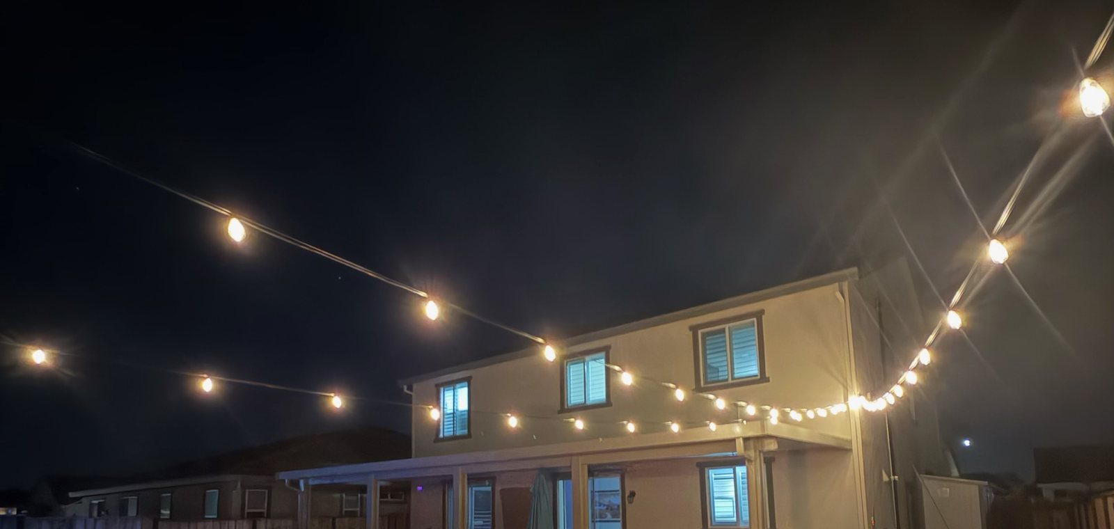 A backyard lit by string lights, landscape lighting and a fire feature installed by Best Diehl Electric